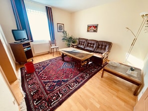Ein Wohnzimmer mit einer Couch, einem Couchtisch, einem roten Teppich, einem Fernseher und einer Heizung.
