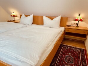 A bedroom with a large bed, two bedside tables with lamps, a wooden headboard, and a patterned rug. - defaultName (Meßstetten-Oberdigisheim)
