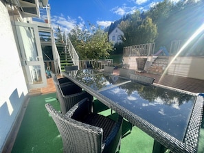An outdoor patio with a glass-top table and wicker chairs, surrounded by a green artificial turf and a white building in the background. - defaultName (Meßstetten-Oberdigisheim)