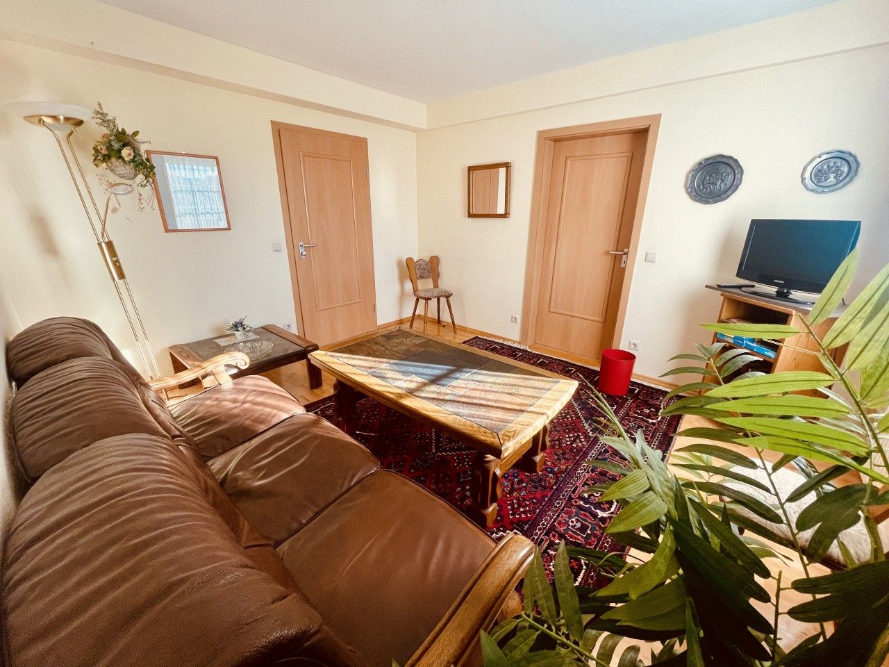 Un salon avec un canapé en cuir marron, une table basse en bois et un téléviseur posé sur un meuble.