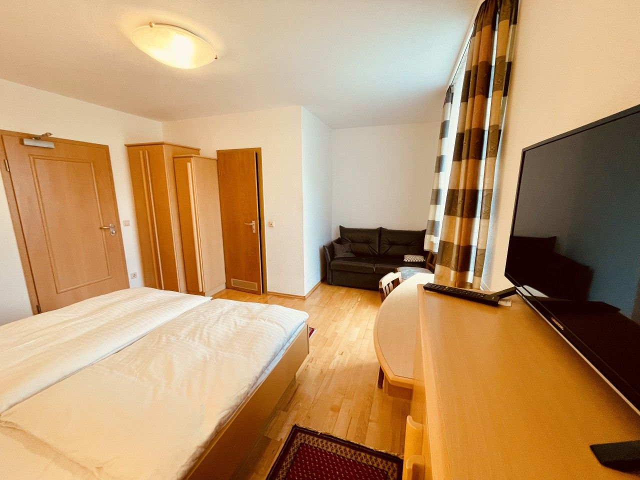 Una habitación de hotel con una cama, un escritorio con computadora, un televisor y un sofá.