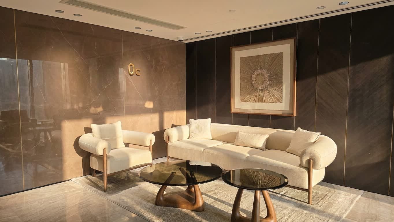 Un salon moderne avec un canapé beige, deux fauteuils et une table basse en verre.