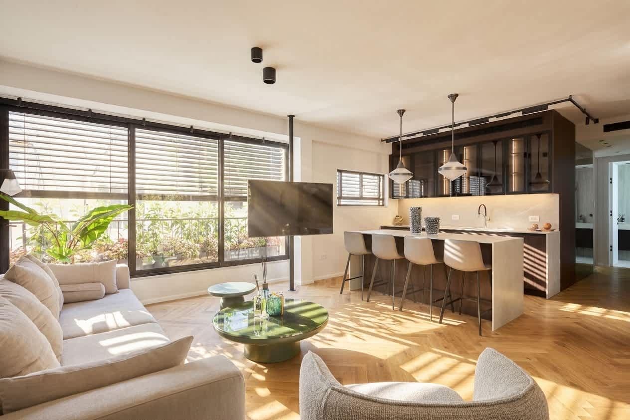 A modern kitchen with a central island, bar stools, and a dining area with a sofa and chairs.