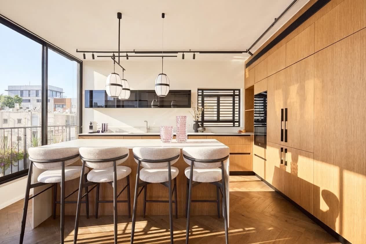 A modern kitchen with a bar area, wooden cabinets, and a large window overlooking the city.