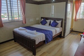 Ein ordentlich bezogenes Bett mit Kopfteil, ein Fenster mit Vorhängen und eine Wand mit Lichtschalter.