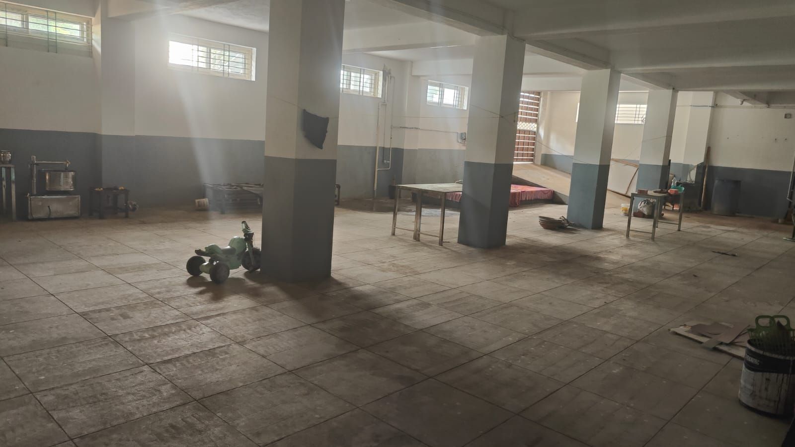A spacious indoor area with tiled flooring, large pillars, and a high ceiling.