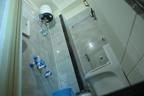 A bathroom with a shower, toilet, and a blue bucket.