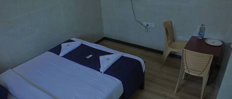 A hotel room with a bed, a desk, a chair, and a television mounted on the wall.