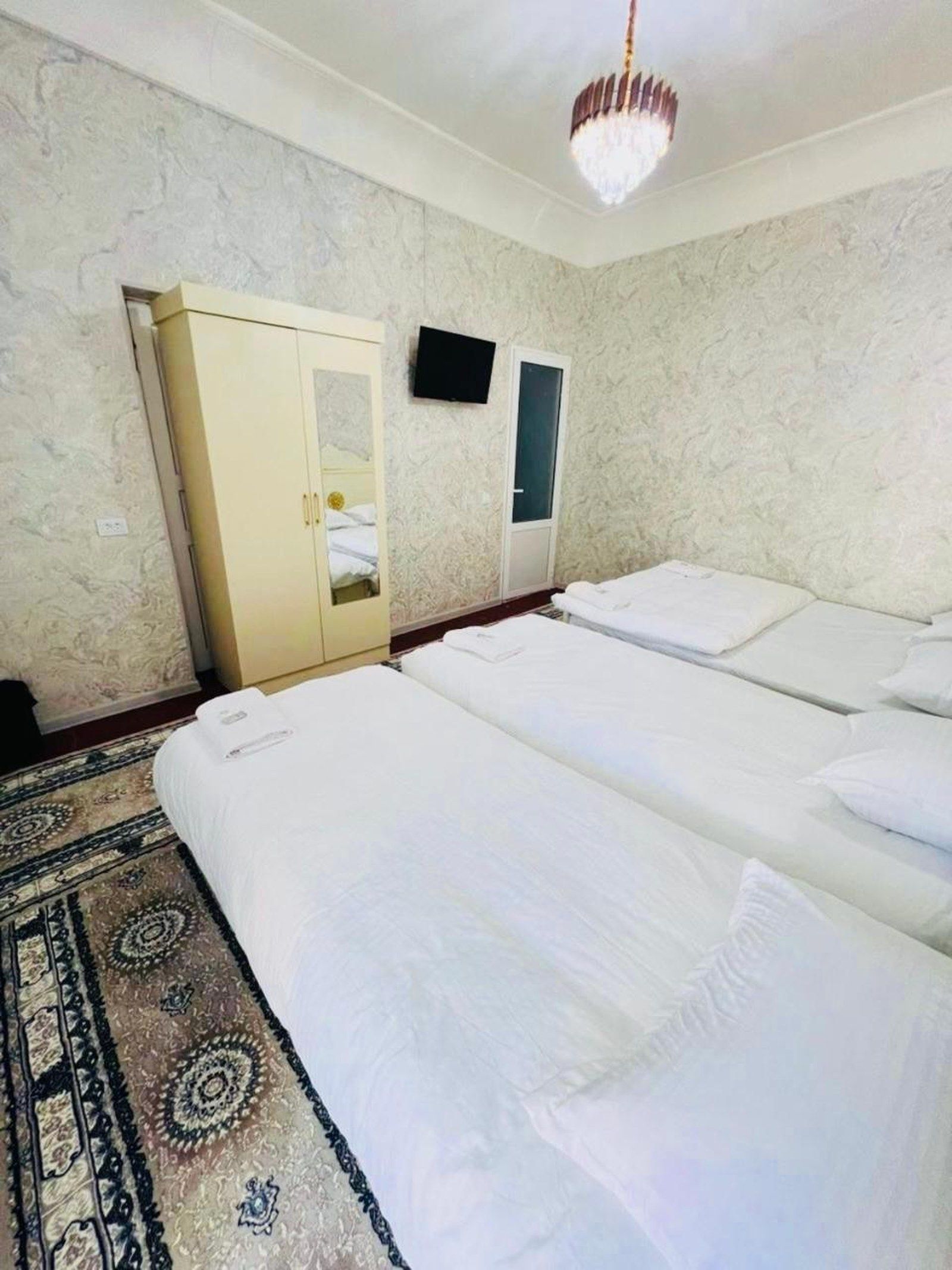 Habitación de hotel con dos camas, un armario, un televisor de pantalla plana y una alfombra estampada.