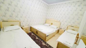Un dormitorio con dos camas individuales, una cama doble y una mesita de noche con lámpara.