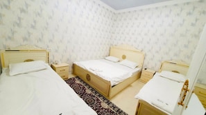 Un dormitorio con dos camas individuales, una cama doble y una mesita de noche con lámpara.
