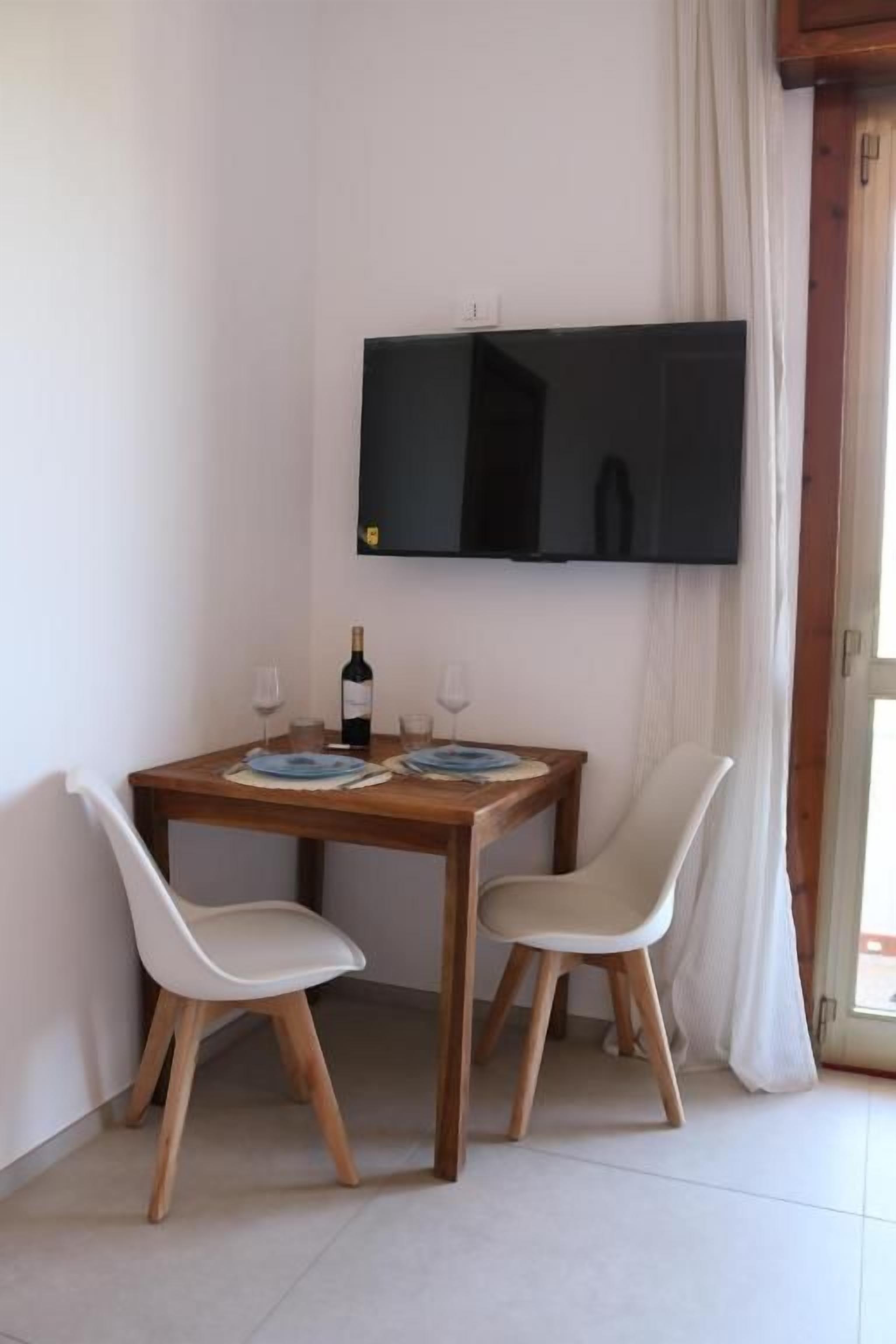 Un comedor con una mesa, dos sillas, una botella de vino y un televisor de pantalla plana montado en la pared.