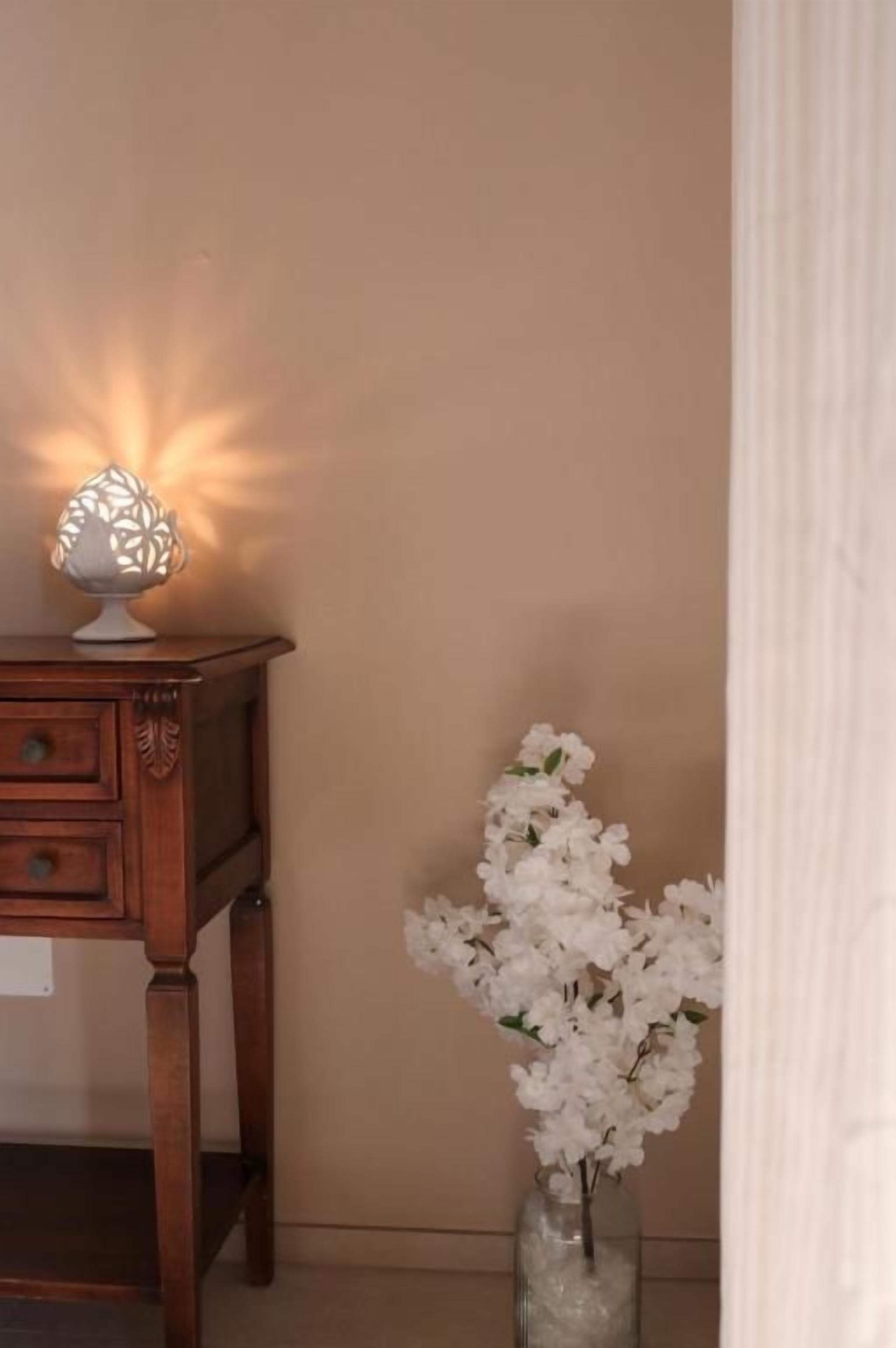 A wooden nightstand with a decorative lamp and a vase of white flowers.