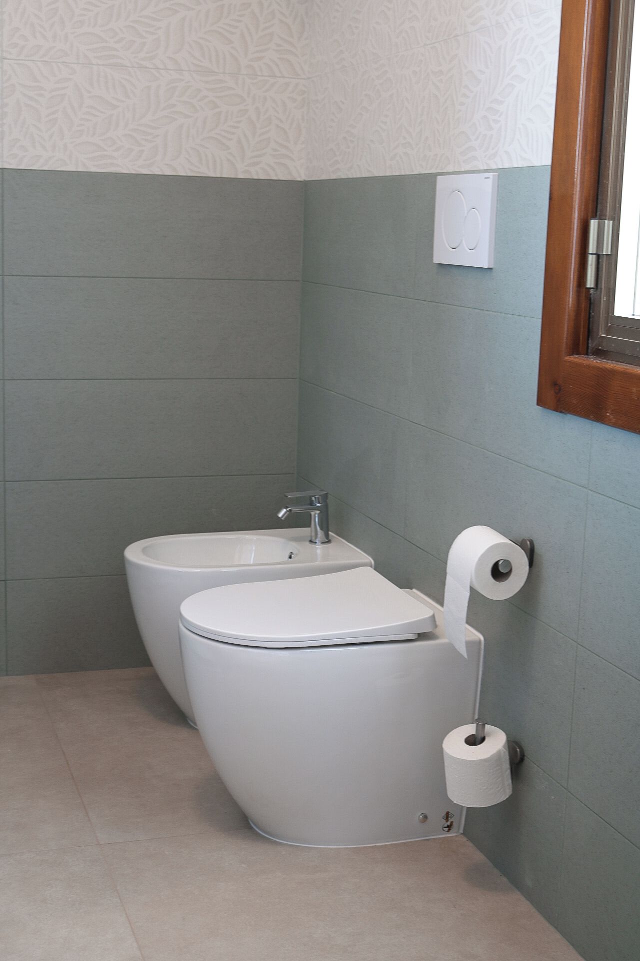 A bathroom with two toilets, a sink, and a toilet paper holder.