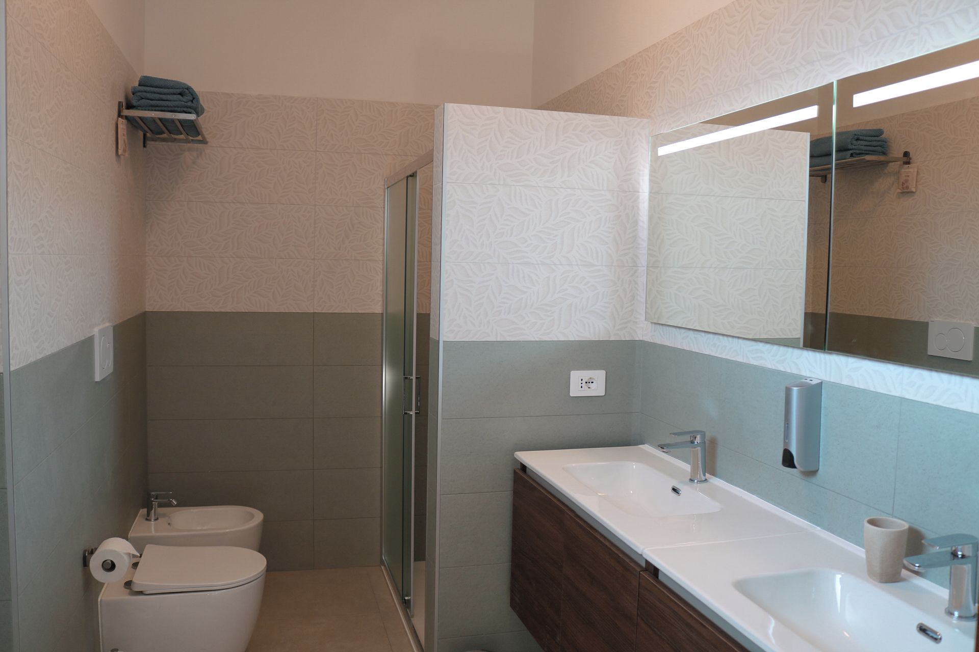 Un baño moderno con ducha, inodoro y lavabo, con azulejos estampados y un espejo grande.