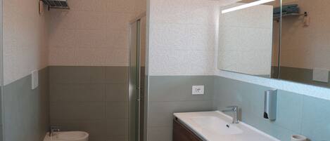 Un baño moderno con ducha, inodoro y lavabo, con azulejos estampados y un espejo grande.