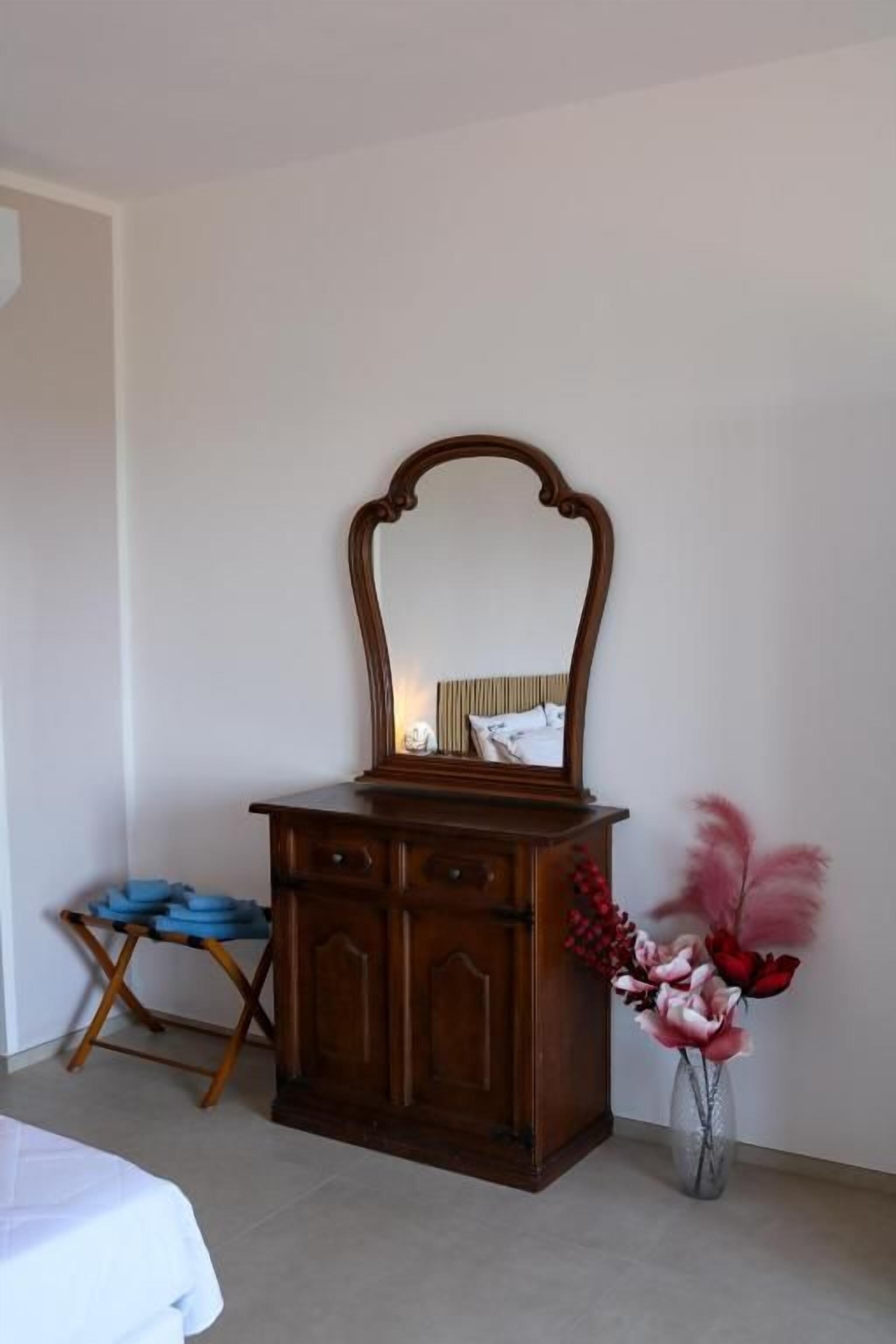 A room with a wooden dresser, a mirror, and a vase with flowers.