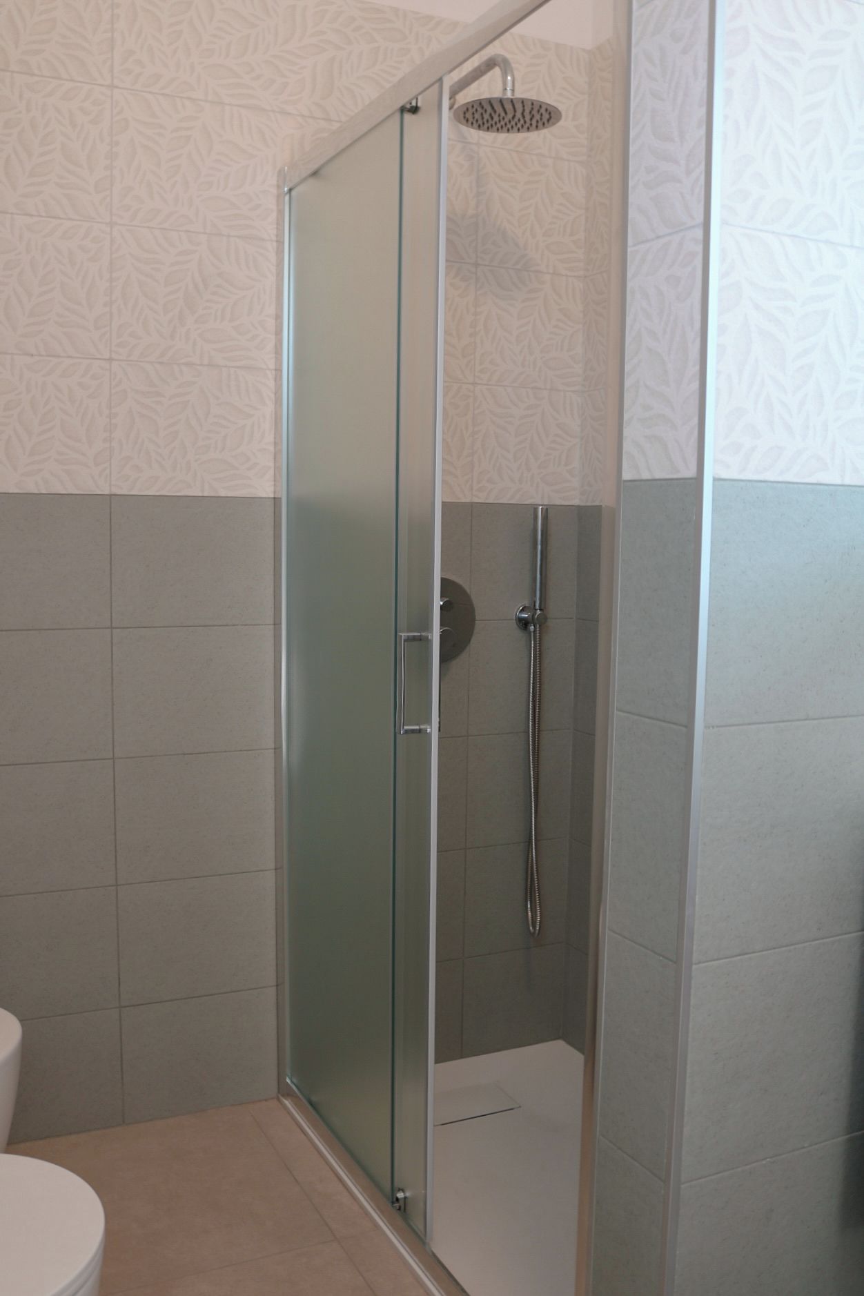 Un box de ducha con paredes de vidrio, un cabezal de ducha de mano, una puerta de vidrio y piso de baldosas.