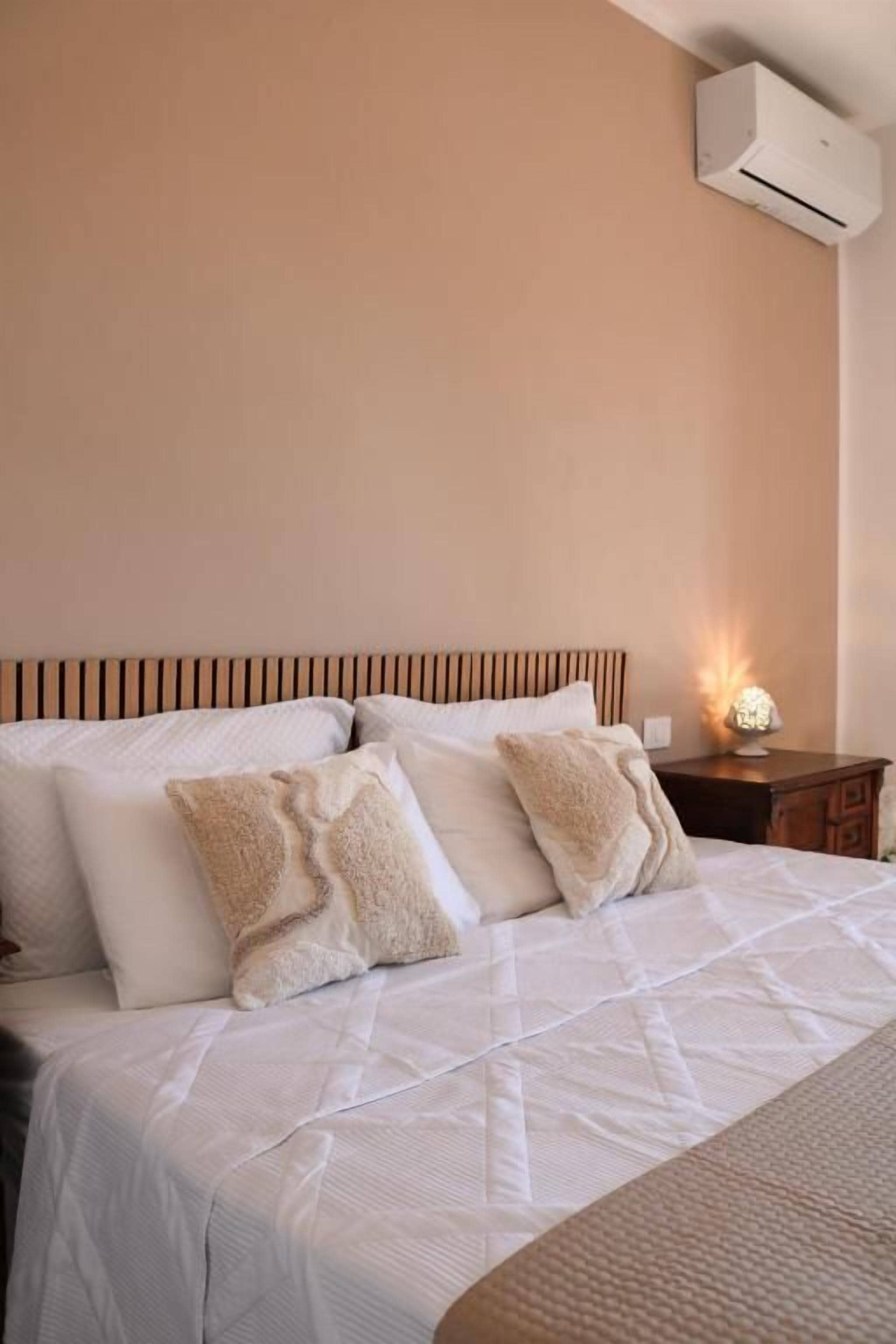 Una cama bien hecha con cabecera a rayas, una lámpara de noche y un aire acondicionado de pared.