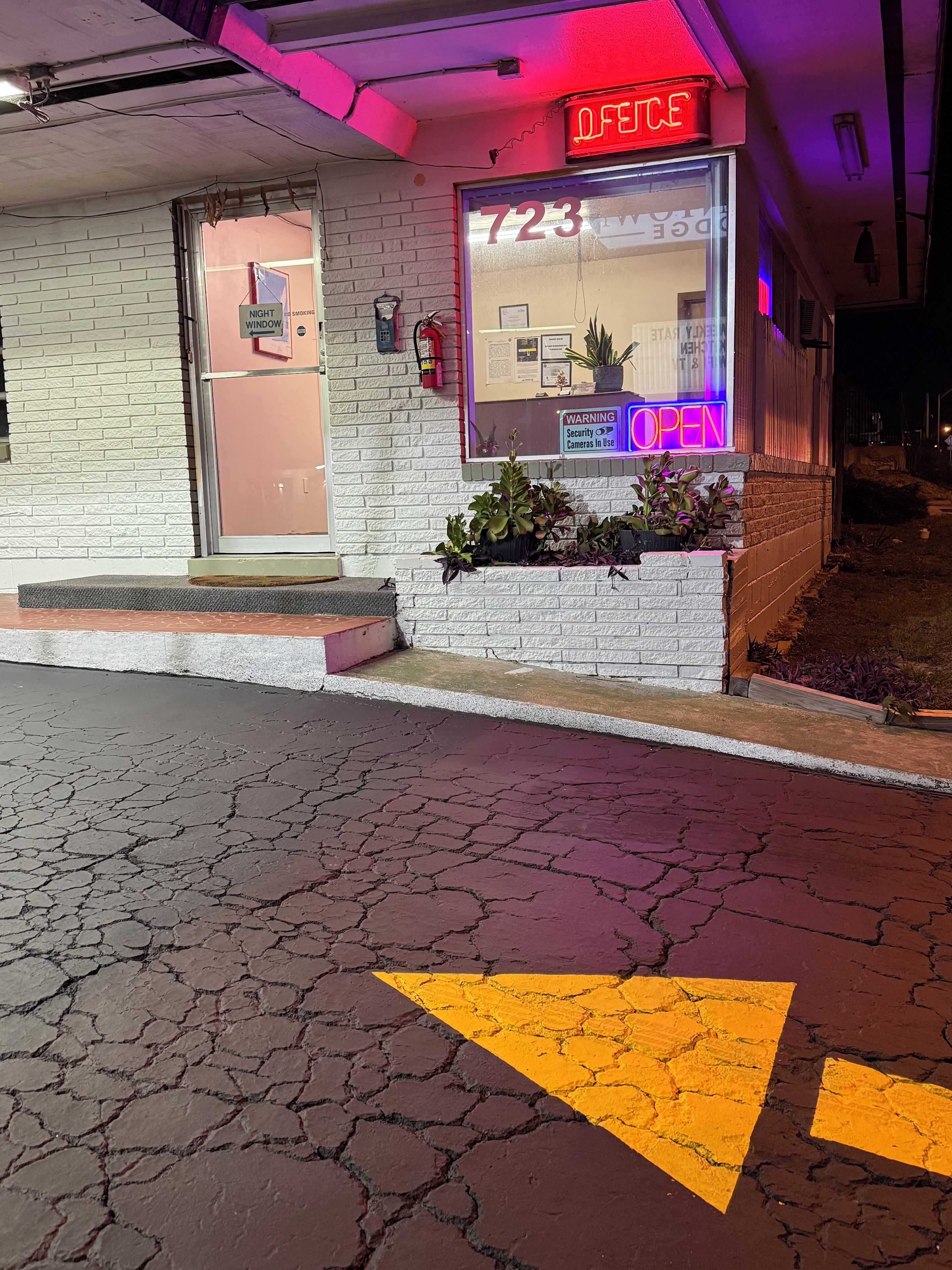 A building with a neon sign indicating it's open, a window with a number, and a warning sign about security cameras.