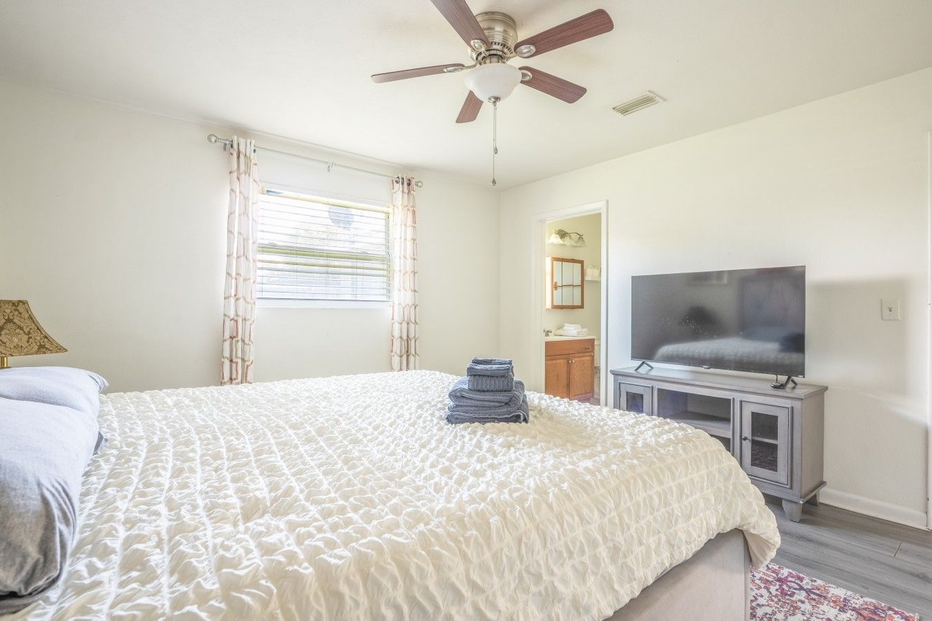 A bedroom with a bed, a ceiling fan, a television, and a window with curtains.