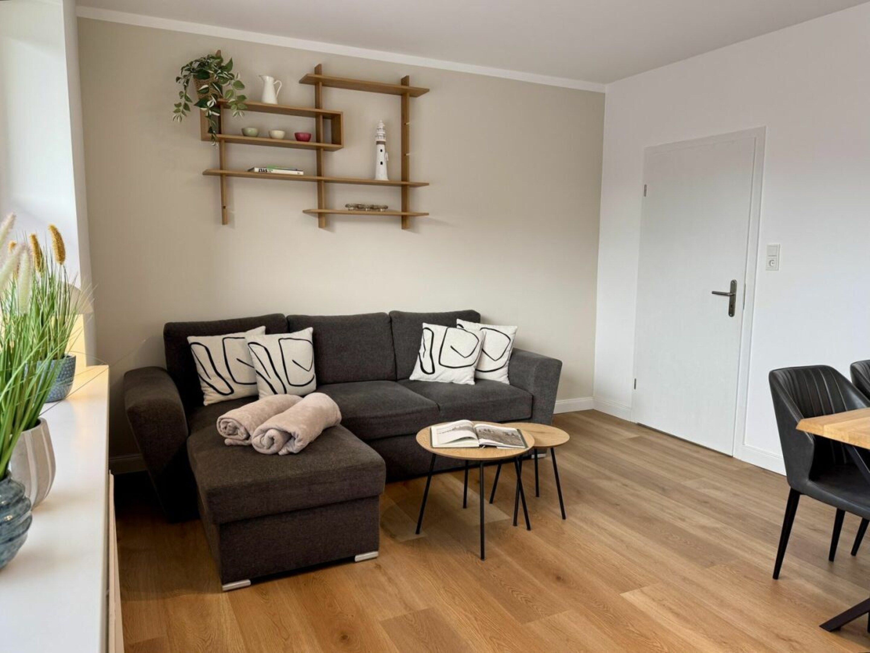Una sala de estar moderna con un sofá gris, una mesita redonda y una estantería de madera con adornos.