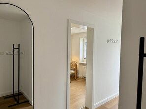 A hallway with a coat rack, a doorway leading to a room with a chair and a radiator, and a sign with text on the wall. - Holiday Apartment With 1 Bedroom (Sylt)