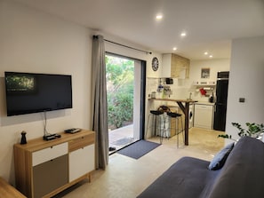 Een moderne woonkamer met een flatscreen televisie, een bank en een eethoek met krukken.