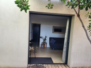 Een open doorgang naar een woonkamer met een bank, een bijzettafeltje en een potplant.