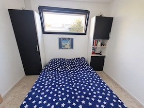 Een slaapkamer met een bed, een raam, een boekenkast en een kledingkast.