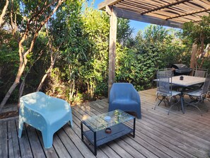Une terrasse extérieure avec une plateforme en bois, une table à plateau en verre et des chaises en plastique bleues.