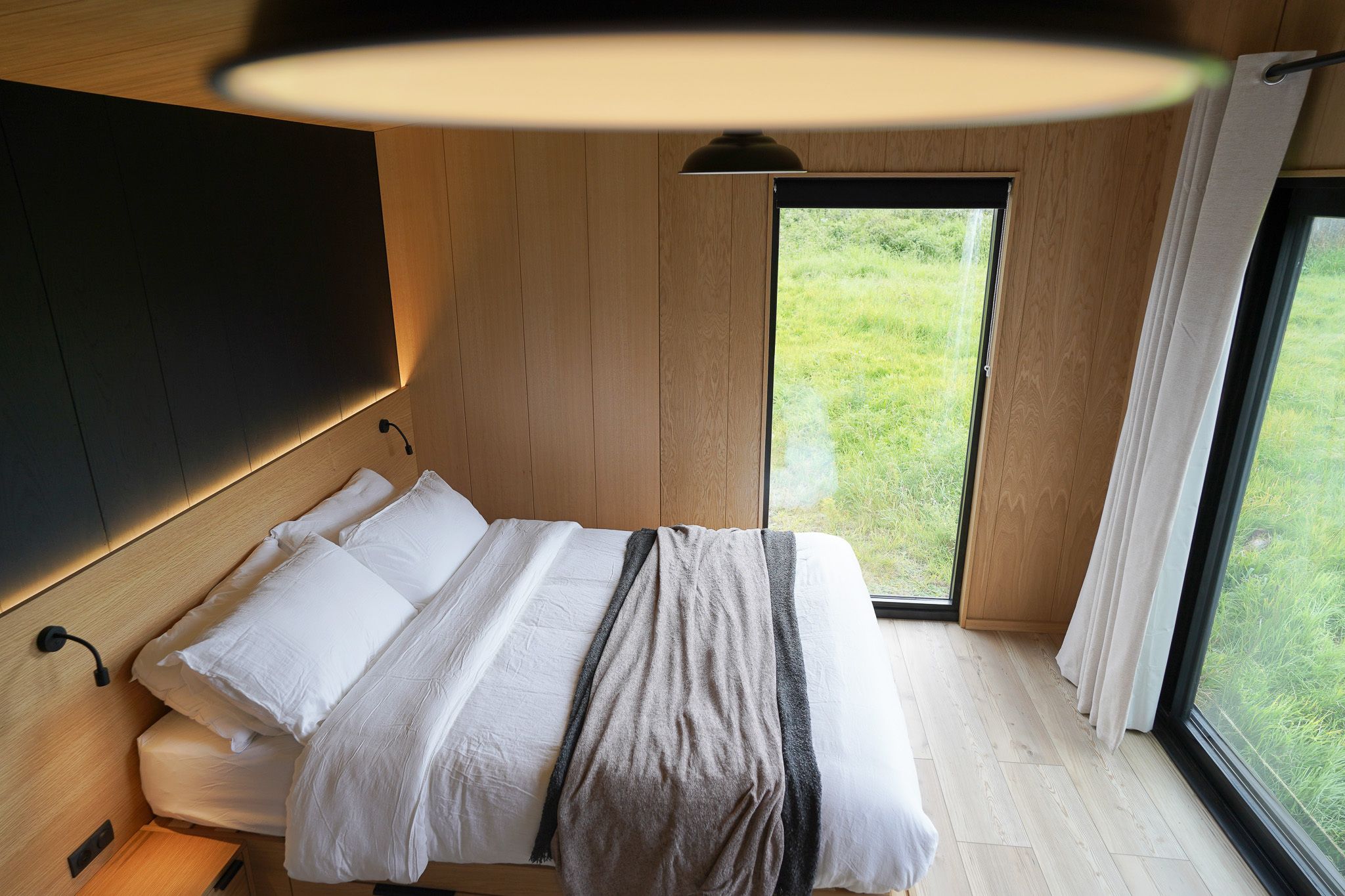 A bedroom with a bed, a bedside table, a lamp, and a window with curtains.