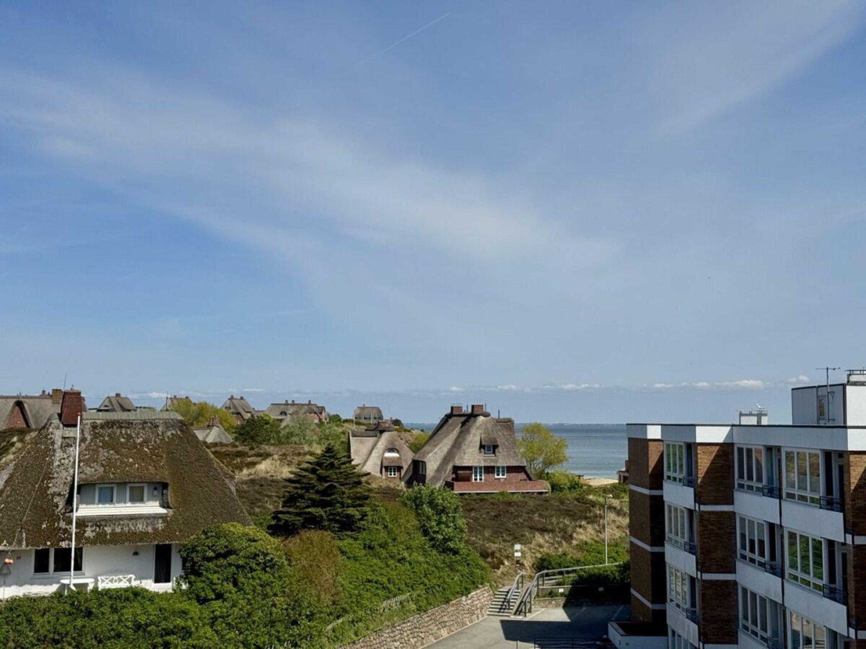 Un quartier résidentiel situé sur la côte, avec des bâtiments à l’architecture traditionnelle et moderne, un ciel dégagé et une vue sur la mer.