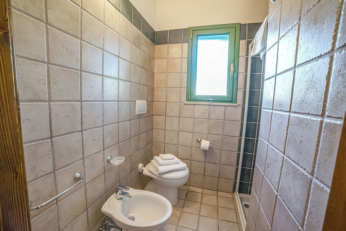 A bathroom with a toilet, bidet, and a window.
