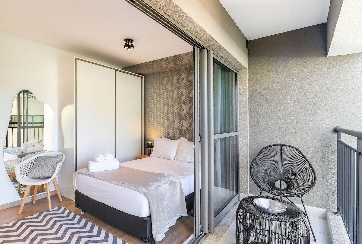 A hotel room with a bed, a desk, a chair, and a balcony with a chair.