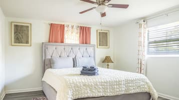 Quarto com cama, ventilador de teto, janela com persianas e duas molduras na parede.