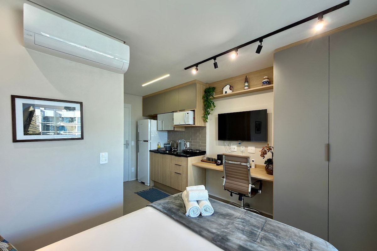 Een kleine hotelkamer met een bed, een bureau, een kitchenette en een televisie.