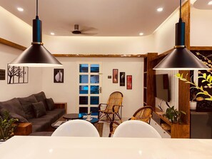 A modern living room with a sofa, dining table, chairs, and two pendant lights. - Kaattil Homes - Luxury Villa & Apartments (Varkala)