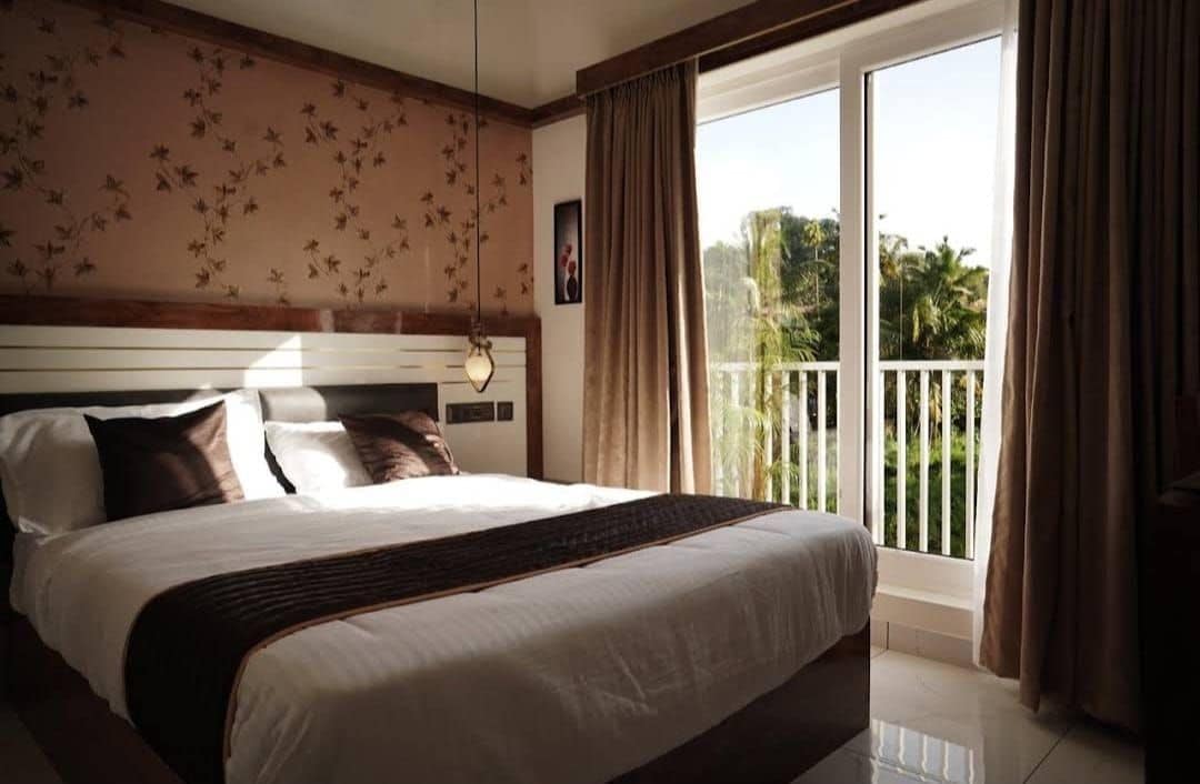 A hotel room with a large bed, a balcony with a view of palm trees, and a floral wallpaper design.