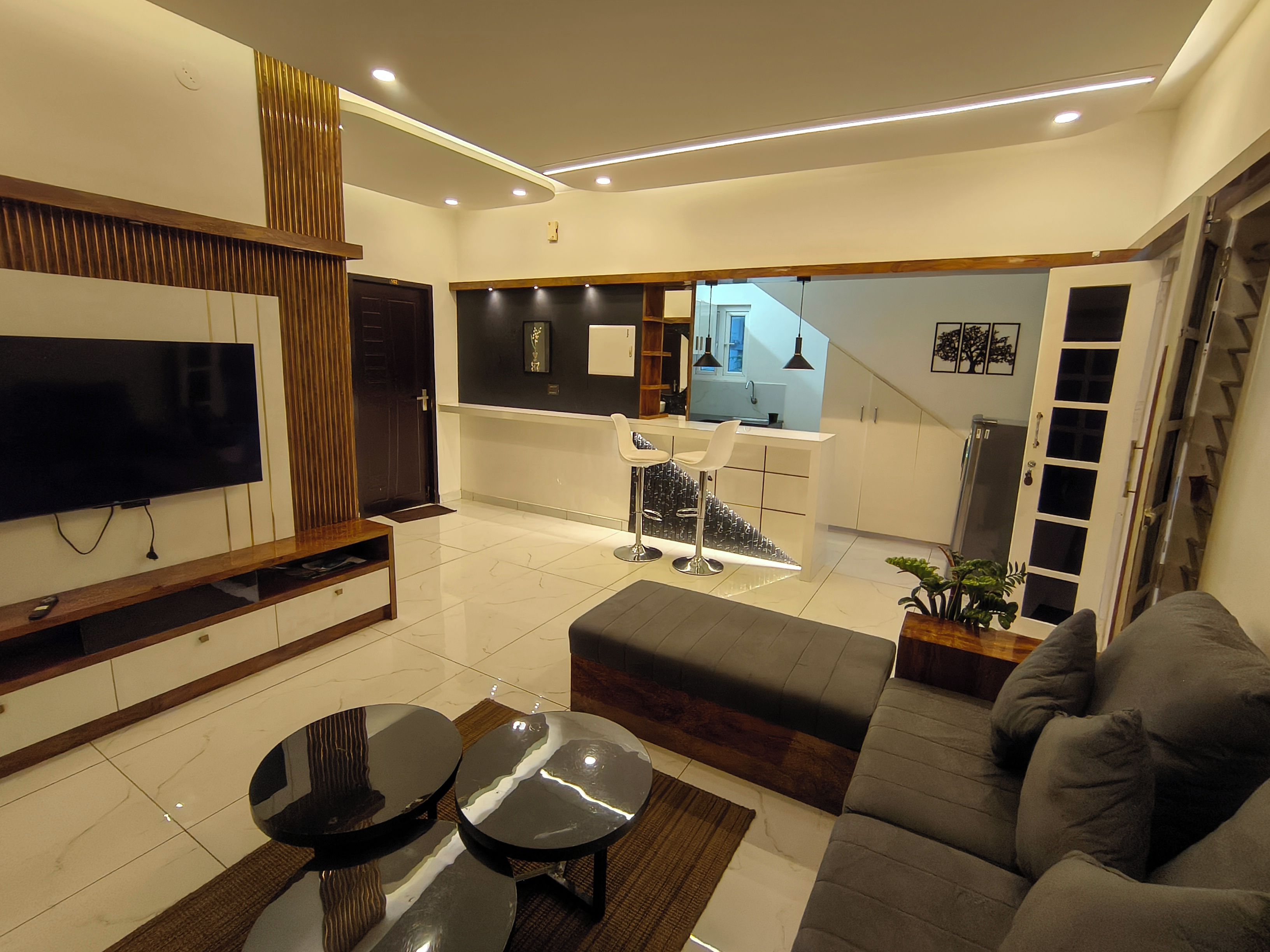 A modern living room with a flat-screen TV, a sofa, a coffee table, and a dining area with a TV and a small table.