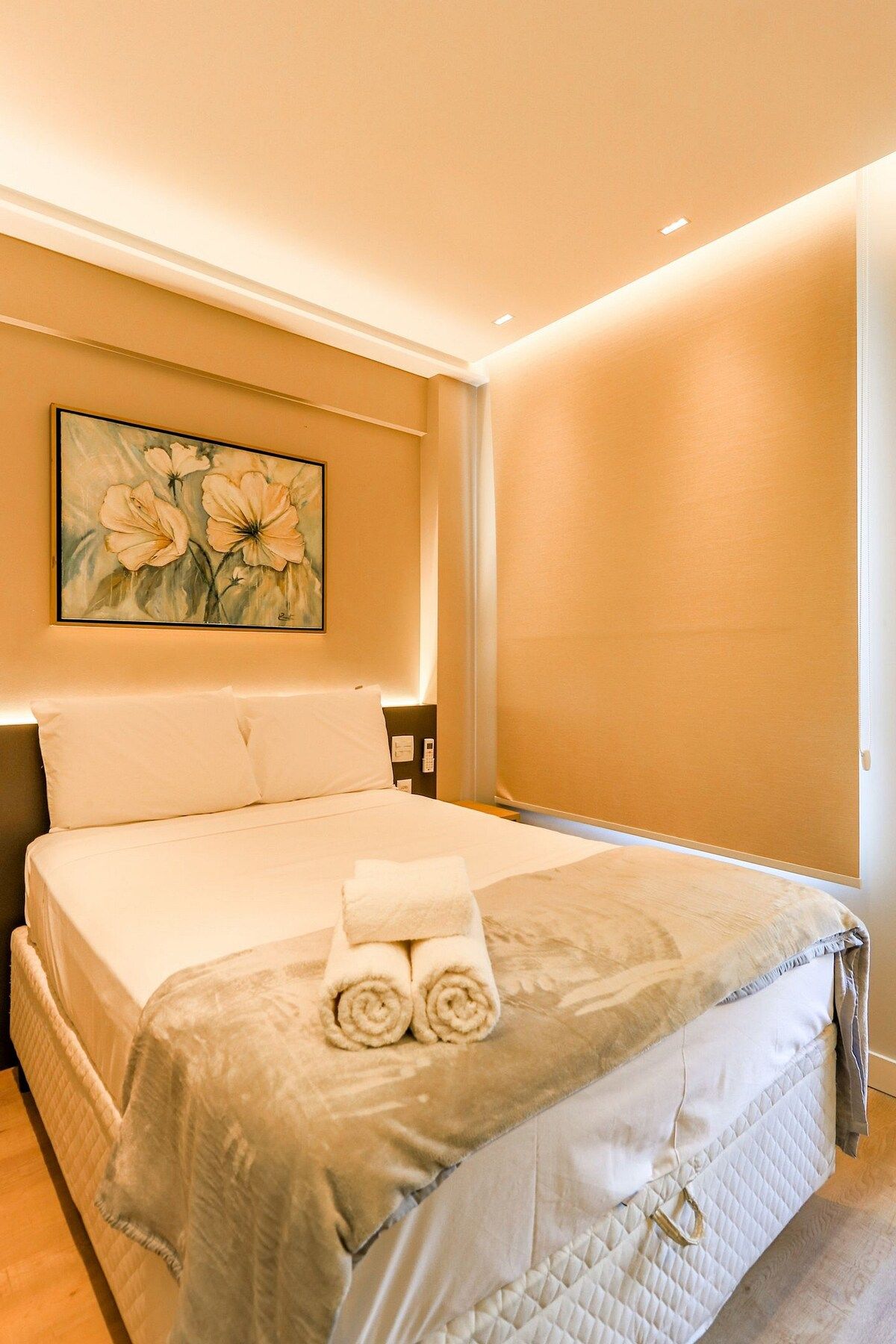 A hotel room with a bed, a painting on the wall, and a bedside table.
