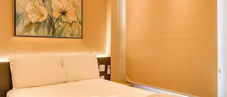 A hotel room with a bed, a painting on the wall, and a bedside table.