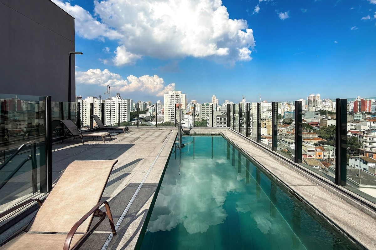A rooftop pool with a city view, lounge chairs, and a glass railing.