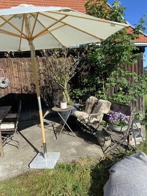Een terras buiten met een tafel en stoelen, een bloempot en een grote parasol.