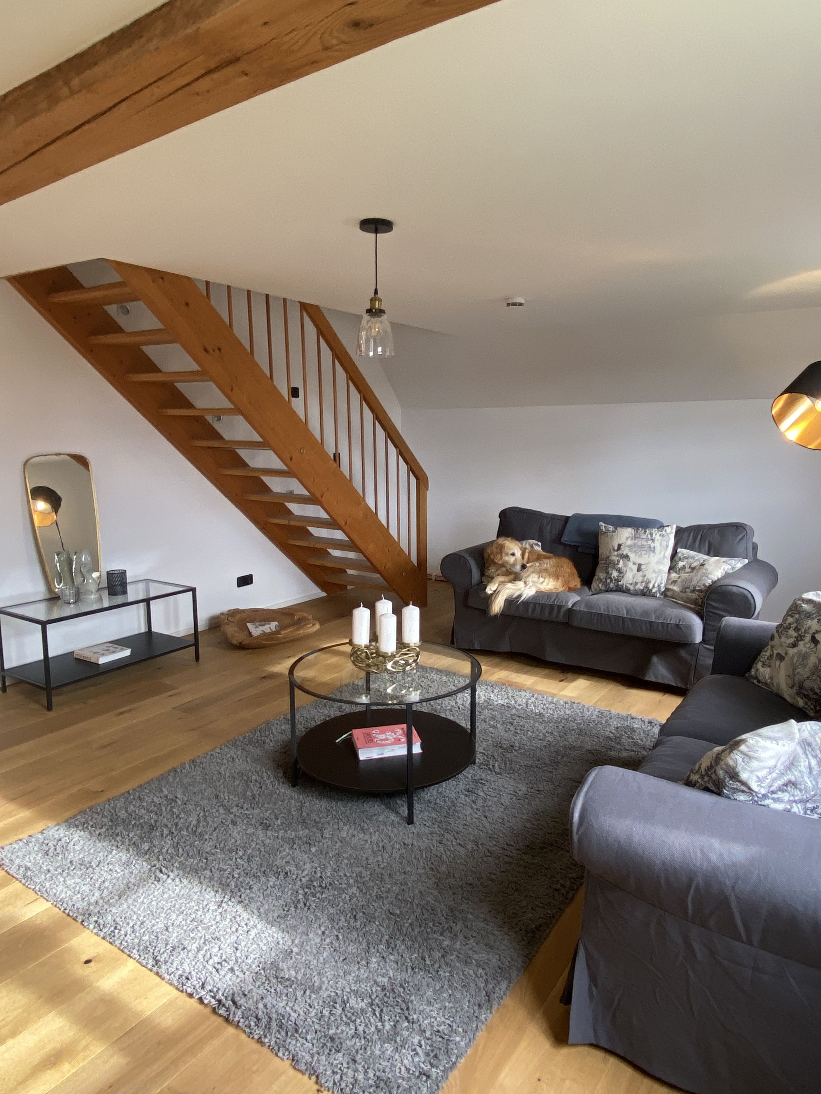 A living room with a staircase, a sofa, a coffee table with candles, and a dog.