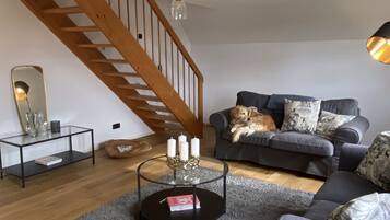 A living room with a staircase, a sofa, a coffee table with candles, and a dog.