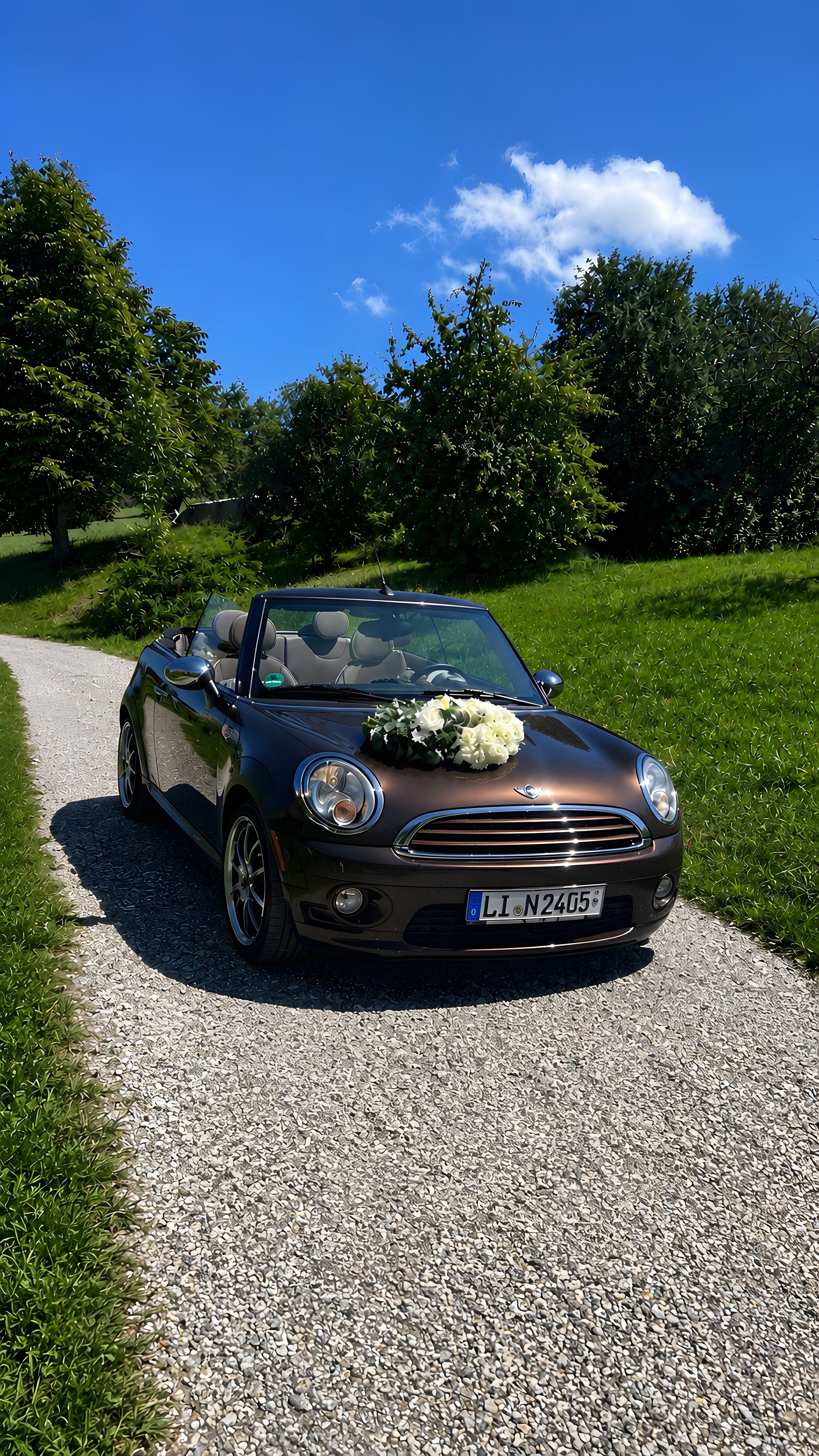 A convertible car parked on a gravel path with a bouquet of white flowers on the hood.