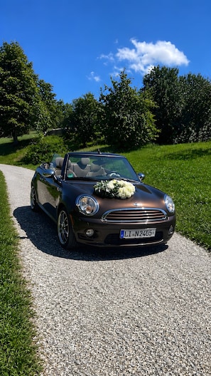 A convertible car parked on a gravel path with a bouquet of white flowers on the hood. - Country House 'Allgäu-Cottage' with Mountain View, Private Terrace and Wi-Fi (Weiler-Simmerberg)