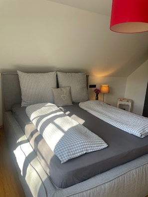 Een bed met geruit beddengoed en kussens, een bedlamp en een rode lamp aan het plafond.