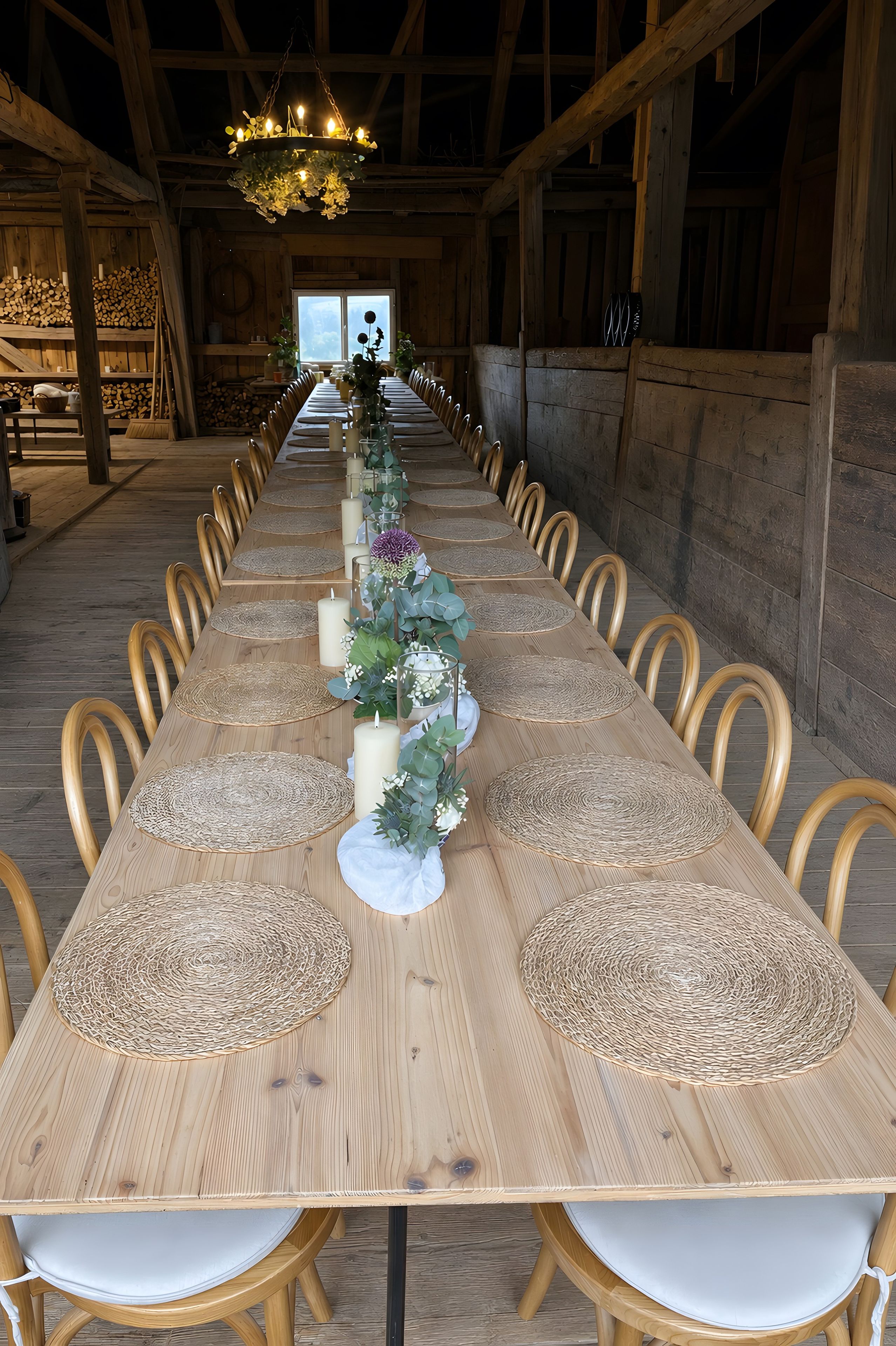 Een lange houten eettafel gedekt met ronde placemats, kaarsen en bloemdecoraties, omringd door houten stoelen in een rustiek interieur.